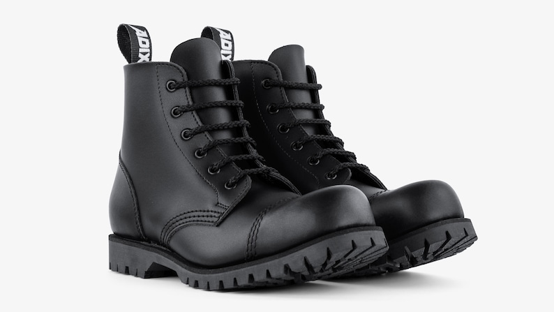 Puede incluir: Un par de botas de combate de cuero negro con dise&ntilde;o de cordones y suela gruesa con tacos. Las botas tienen punta redondeada y una leng&uuml;eta en la parte trasera con la palabra "ADIX" impresa.