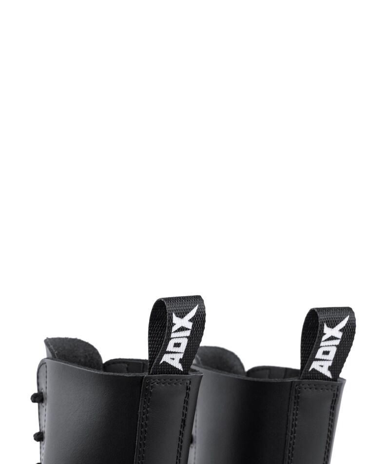 Puede incluir: Primer plano de dos botas de cuero negro. Cada bota tiene una leng&uuml;eta con la palabra "ADIX" en blanco. Las botas tienen costuras y cordones visibles. El fondo es blanco.