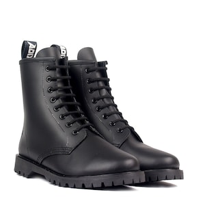 May include: A pair of black combat boots with a matte finish. The boots have black laces, a rounded toe, and a thick, ridged sole. The pull tab at the top of the boot features white text. The boots are set against a white background.