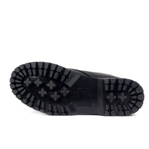 May include: Black boot sole with a rugged, textured tread pattern. The sole is made of a durable material and features a series of deep grooves and geometric shapes for traction. The boot sole is designed for outdoor use.
