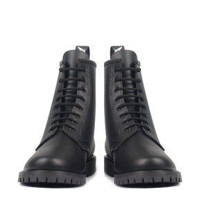May include: A pair of black combat boots with a lace-up design. The boots have a rounded toe, a thick lug sole, and a small tab at the top of the boot. The boots are made of a smooth, matte material.