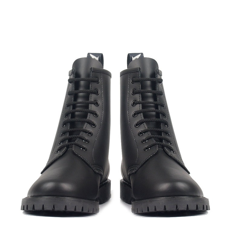 May include: A pair of black combat boots with a lace-up design. The boots have a rounded toe, a thick lug sole, and a small tab at the top of the boot. The boots are made of a smooth, matte material.