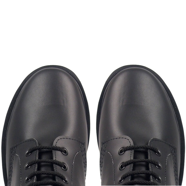 May include: A top-down view of two black leather boots with black laces. The boots have a rounded toe and a textured rubber sole. The boots are set against a white background.