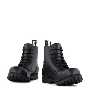 May include: Pair of black leather combat boots with thick soles and black laces. The boots have a rounded toe and a pull tab at the back with the word "ADI" printed on it. The boots are set against a white background.