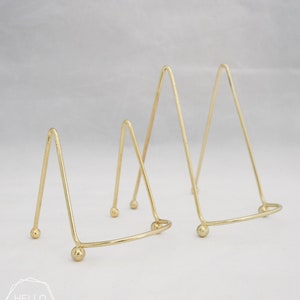 May include: Two gold metal triangular display stands with rounded bases. The stands are different sizes.