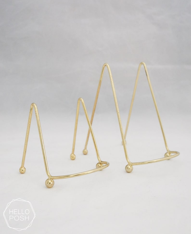 May include: Two gold metal triangular display stands with rounded bases. The stands are different sizes.