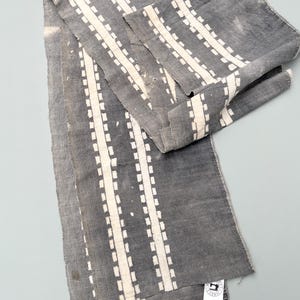 May include: Gray fabric with a white geometric pattern. The fabric is folded and has a small white tag with the text "Sew Much Fabric" and social media icons.
