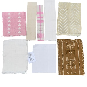 May include: An assortment of fabric swatches in various colors and patterns. Includes pink with white triangles, beige, white, and brown with geometric designs. Some pieces have fringed edges, and one has a tag.