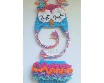 May include: A crocheted owl hat with a flower on top and a matching crocheted diaper cover with colorful ruffles. The hat and diaper cover are made in shades of blue, pink, orange, purple, and green.
