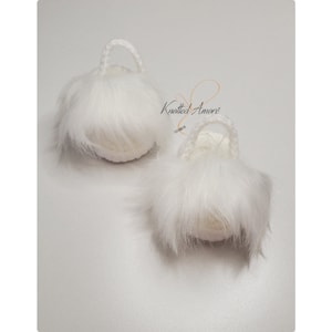 May include: Two white crocheted pom pom bags with handles. The bags are made with a fluffy white yarn and have a small, round shape.