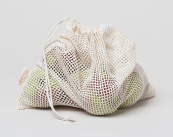 Può includere: Una borsa di rete bianca per prodotti, con chiusura a coulisse, piena di mele verdi. La borsa ha un'etichetta rossa che dice "Planet Friendly".