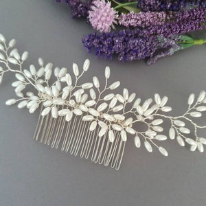 May include: A silver hair comb with a delicate design of white pearl beads arranged in a floral pattern.
