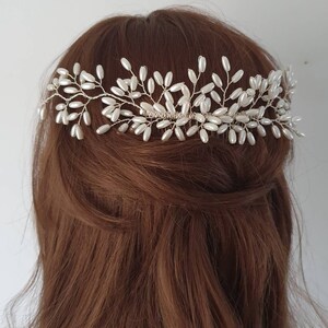 May include: A pearl and wire hair comb with a delicate floral design. The comb is made of silver wire and features small, white pearls.