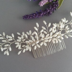 May include: A silver hair comb with a delicate design of white pearl beads arranged in a floral pattern.