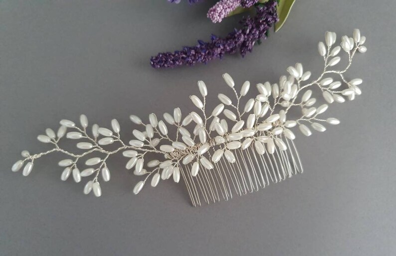 May include: A silver hair comb with a delicate design of white pearl beads arranged in a floral pattern.