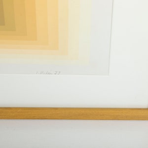 May include: A framed abstract print with a geometric pattern of yellow, orange, and brown hues. The print is signed "L. Wilson 77" in the bottom right corner.