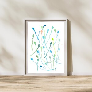 May include: A framed watercolor print featuring an abstract design of elongated shapes in shades of blue, green, and a touch of peach. The artwork is displayed against a white background, with a wooden floor visible below.