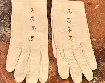 Puede incluir: Un par de guantes color crema con delicados bordados florales en rojo, azul y rosa. Los guantes están hechos de un material suave y presentan un diseño clásico, perfecto para añadir un toque de elegancia.