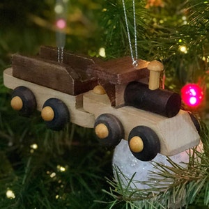 May include: A wooden toy train ornament with a brown boxcar and a black engine. The train has six wheels and is decorated with a silver string for hanging on a Christmas tree.
