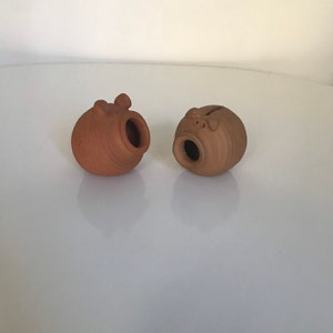 Puede incluir: Dos alcancías de terracota con una superficie texturizada. Una alcancía tiene una abertura redonda en el lateral, mientras que la otra tiene una ranura en la parte superior.