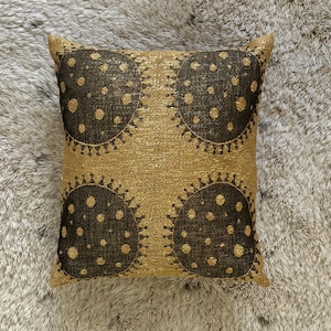 Puede incluir: Una almohada de tiro dorada con un patrón geométrico negro. El patrón presenta cuatro círculos grandes con círculos más pequeños dentro.