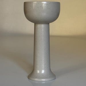 May include: A speckled white ceramic vase with a wide, rounded top and a tall, slender base.