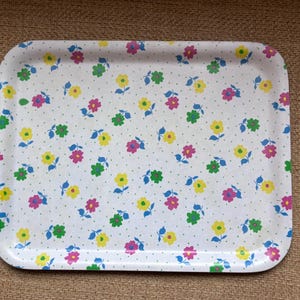 May include: A rectangular serving tray with a white background featuring a repeating pattern of small pink, yellow, and green flowers with blue leaves. The surface is covered in tiny blue dots scattered between the floral motifs.