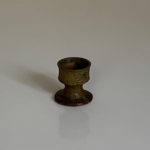 Puede incluir: Un pequeño cáliz de cerámica marrón con una superficie texturizada y una base ancha.
