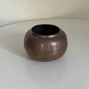 Könnte beinhalten: Ein runder, gehämmerter Kupfertopf mit einer dunkelbraunen Patina.