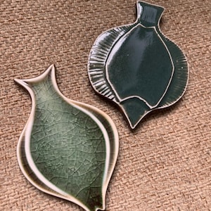 May include: Two green ceramic dishes shaped like fish. The dishes have a crackled glaze and a white rim.