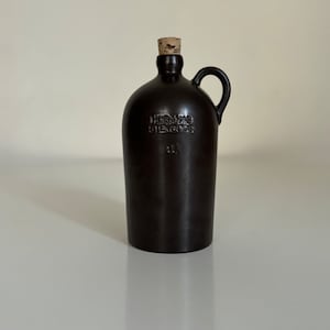 May include: A brown ceramic bottle with a cork stopper and a handle. The bottle is labeled "HCGANAS STENGODS 1L".