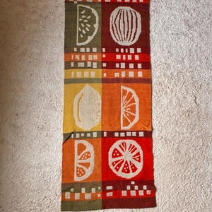 Puede incluir: Un camino de mesa largo y rectangular para la cocina con un diseño de frutas coloridas. El camino de mesa presenta un patrón repetitivo de limones, naranjas y sandías en tonos de rojo, naranja, amarillo y verde.