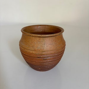 Può includere: Un piccolo vaso in ceramica marrone con una superficie testurizzata e rigata.