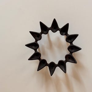 以下が含まれることがあります： 12個の涙型の個別のキャンドル用スロットを持つ黒い金属製のキャンドルホルダー。ホルダーは円形で、スターバーストのデザインです。