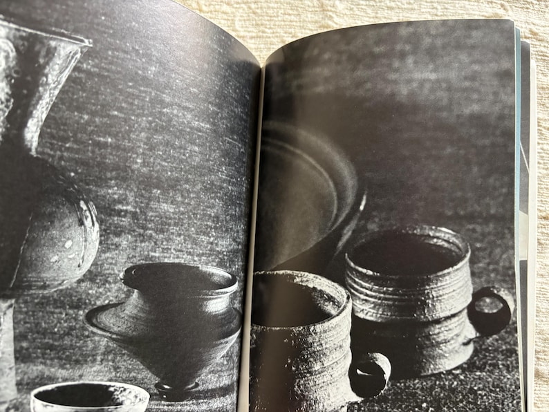May include: Black and white photograph of various ceramic vessels. The image includes a tall vase, a round vessel, a small bowl, and two mugs with handles. The vessels have a textured, rustic appearance.