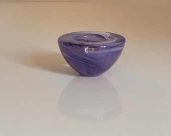 May include: A small, decorative glass bowl with a rounded shape. The bowl is a deep purple colour with swirling white patterns throughout the glass. The bowl is on a white surface.