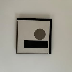 以下が含まれることがあります： 白い背景に黒い枠で囲まれたプリント。2つの幾何学的な形が描かれている。黒い長方形が茶色の円の下にある。