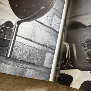 May include: Black and white image of a wall-mounted lamp with a perforated shade and a curved, metallic arm. The lamp is attached to a brick wall. The image also shows a portion of a second lamp.