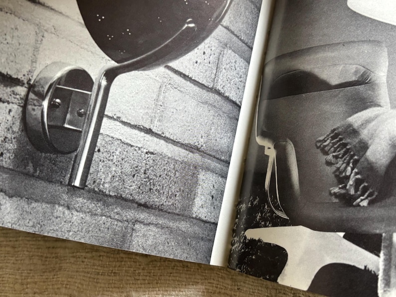 May include: Black and white image of a wall-mounted lamp with a perforated shade and a curved, metallic arm. The lamp is attached to a brick wall. The image also shows a portion of a second lamp.