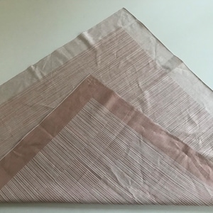 Puede incluir: Una tela de rayas beige y marrón con un borde beige. La tela está doblada en forma triangular.