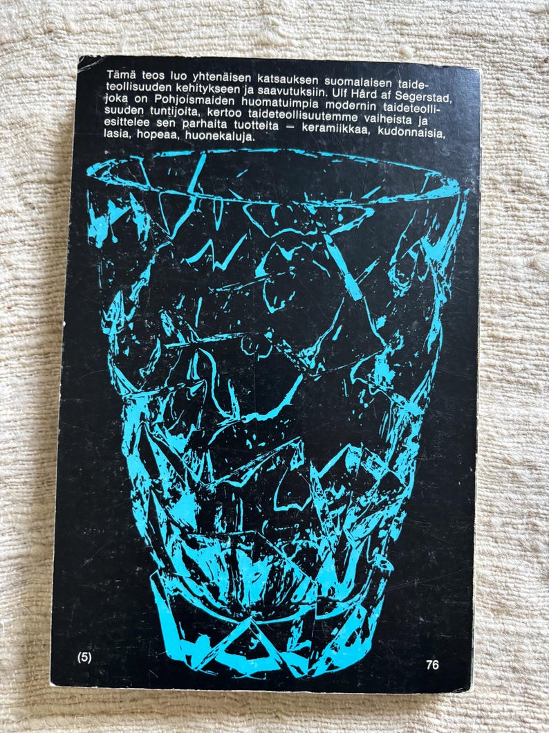 May include: A book cover featuring a black background with a turquoise geometric design of a vase. The cover includes text in Finnish, with the number 76 at the bottom right and the number 5 in parentheses at the bottom left.