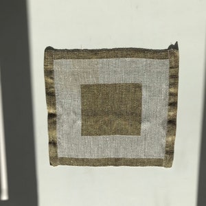 Puede incluir: Un posavasos cuadrado de lino de color blanco roto con un cuadrado de lino marrón en el centro. El posavasos tiene un borde marrón.