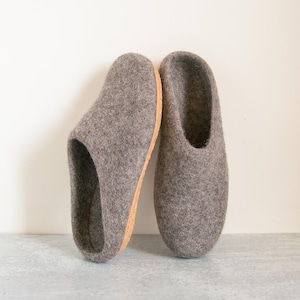 May include: A pair of grey felt slippers with a cork sole. The slippers are a muted grey colour and have a simple, minimalist design. The cork sole provides a natural contrast to the felt upper.