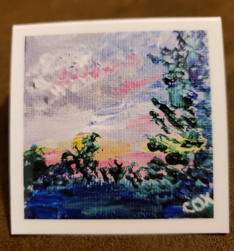 May include: A painting of a sunset over a forest with a pink and yellow sky. The trees are green and blue, and there is a white cloud in the sky. The painting is signed "COX" in the bottom right corner.