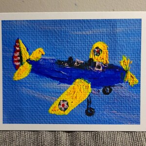 Könnte beinhalten: Ein blaues und gelbes Flugzeugbild auf einer Leinwand. Das Flugzeug hat einen gelben Propeller und ein gelbes Cockpit. Der Hintergrund ist hellblau.