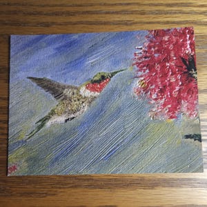 May include: A painting of a hummingbird in flight with a red and pink flower in the background. The hummingbird is painted in shades of green, brown, and red. The background is a blue and green wash.
