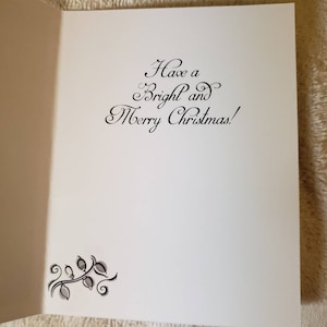 May include: An open white Christmas card featuring the message "Have a Bright and Merry Christmas!" in black script. A decorative floral design is in the lower left corner. The card is displayed open, showing the inside.