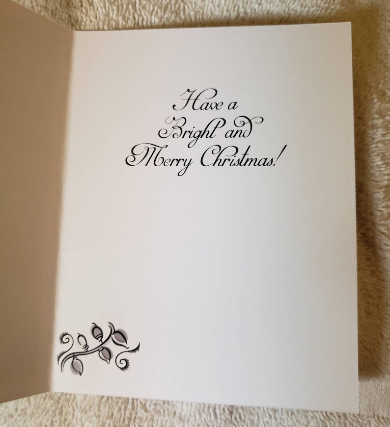 May include: An open white Christmas card featuring the message "Have a Bright and Merry Christmas!" in black script. A decorative floral design is in the lower left corner. The card is displayed open, showing the inside.