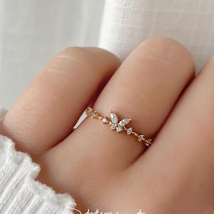May include: A gold ring featuring a dainty chain and a small butterfly design adorned with clear cubic zirconia stones.