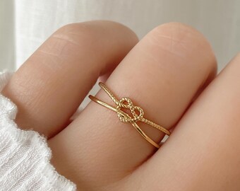 Puede incluir: Anillo de oro con un diseño de nudo. El anillo es fino y delicado, y el nudo es un diseño simple y elegante.